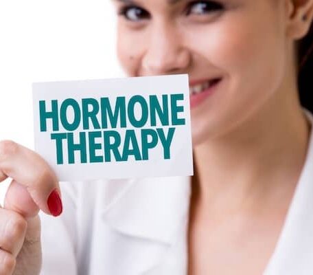 A smiling healthcare professional holding a card that reads "Hormone Therapy" to promote endocrine health services.