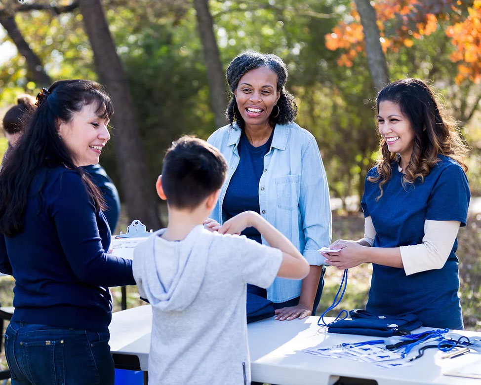 A group of diverse health volunteers interacting with a young boy and his family at an outdoor community health fair table.