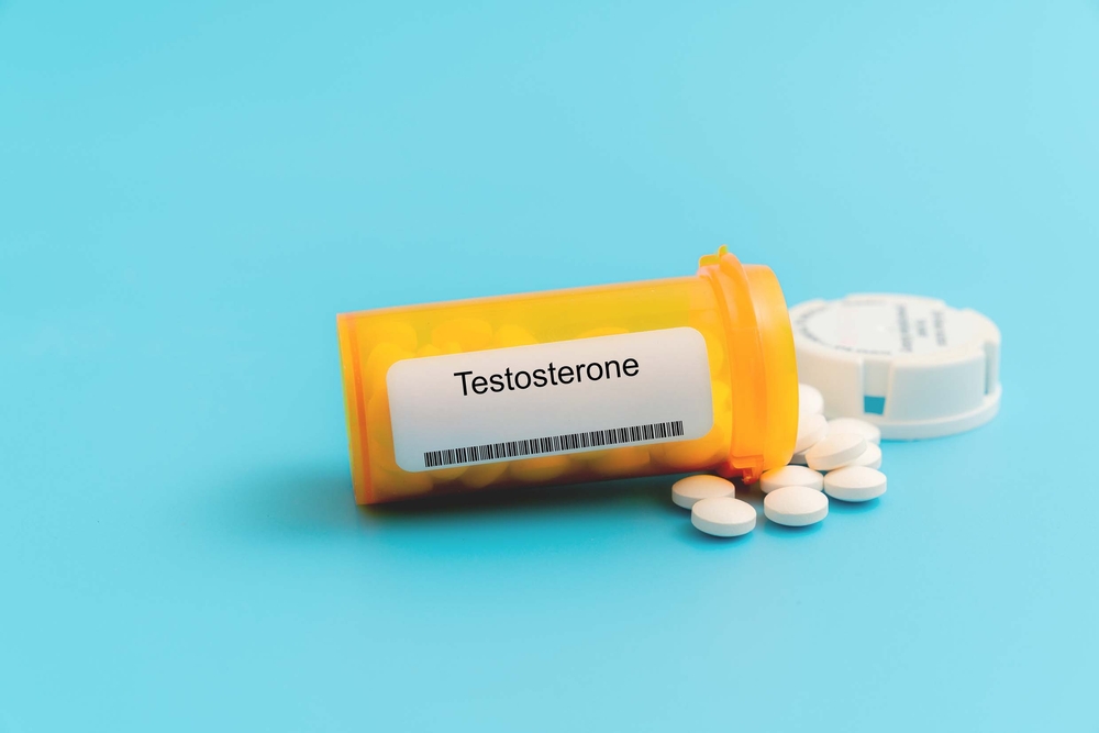 An amber prescription pill bottle labeled "Testosterone" with white tablets spilled out on a blue background.