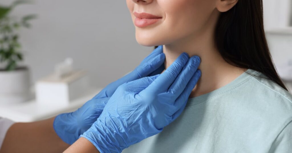 Close-up of a healthcare provider in blue medical gloves performing a physical palpation exam on a patient's thyroid gland.