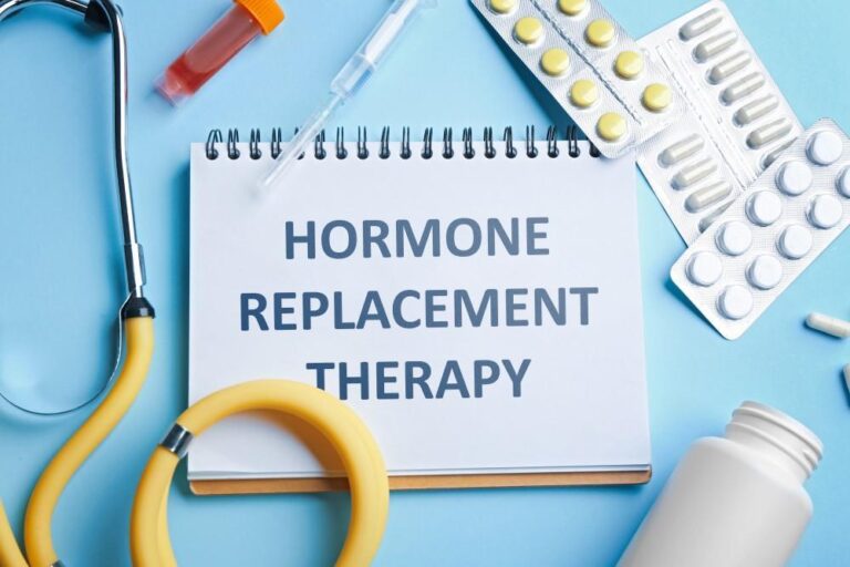 A white notebook with the text 'HORMONE REPLACEMENT THERAPY' surrounded by a yellow stethoscope, pill blisters, and medical supplies on a blue background.