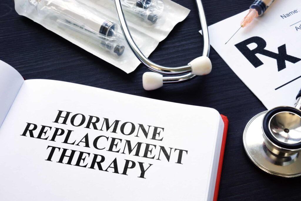 An open book with the text 'HORMONE REPLACEMENT THERAPY' next to a stethoscope, syringes, and a medical prescription pad.