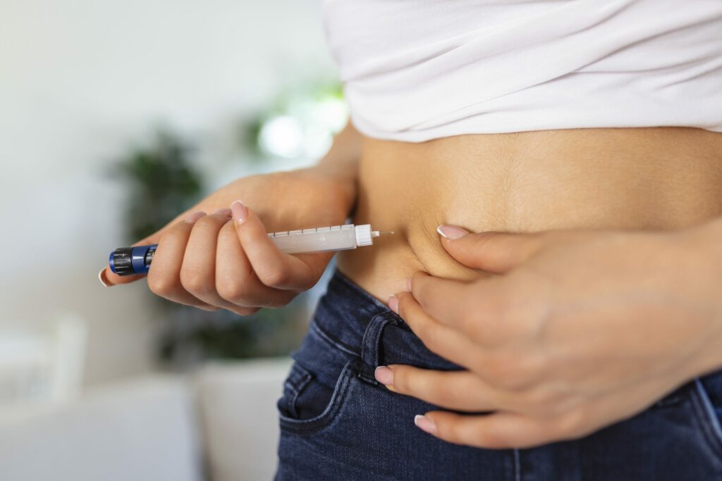 A person administering a subcutaneous injection into the abdomen using an insulin pen, showing the pinching of skin for proper needle entry.